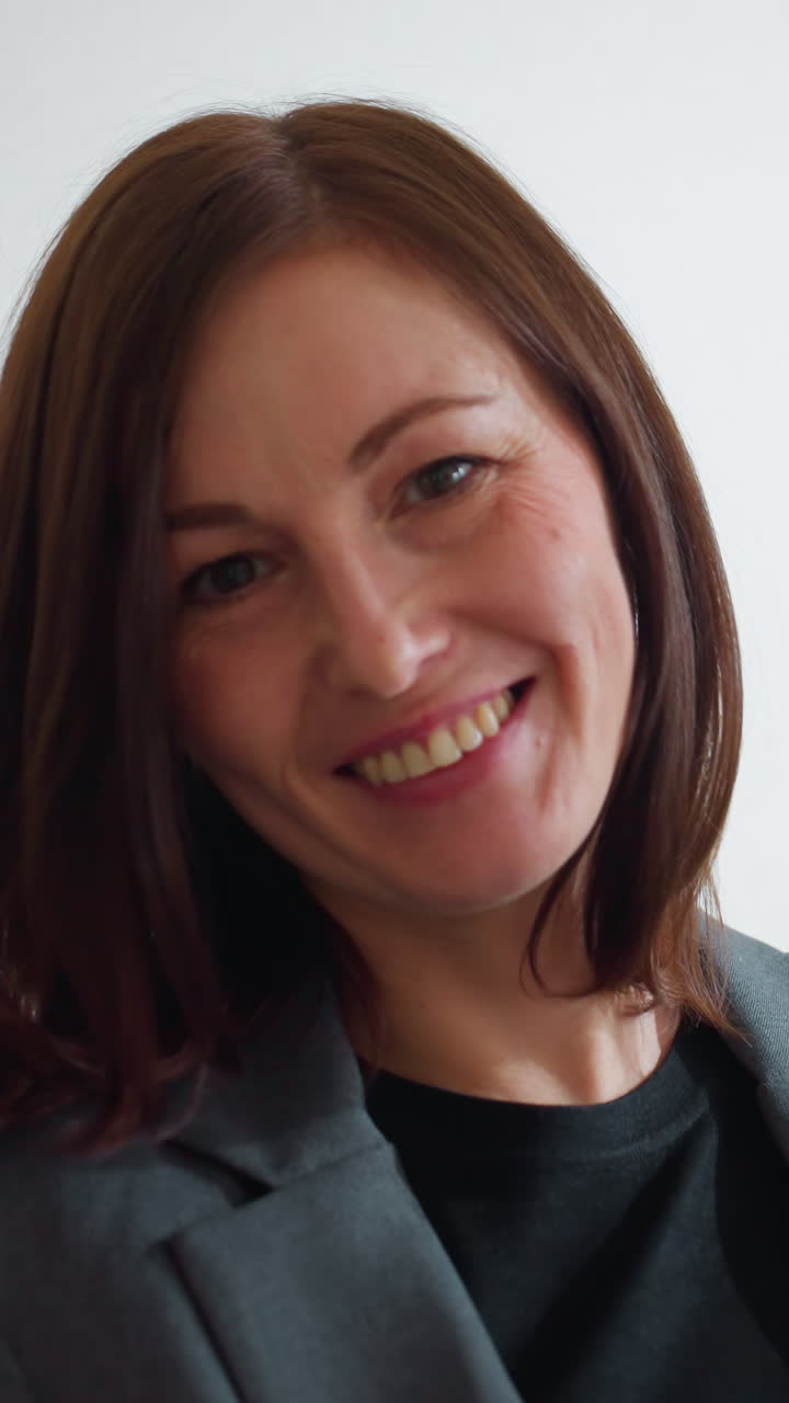 Confident businesswoman in formal suit sitting on couch using digital tablet in modern office lounge surrounded by green indoor plants while reading or browsing calmly in natural daylight