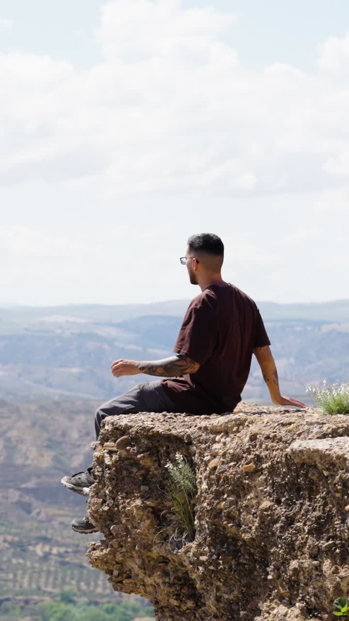 Tourist sitting on cliff edge, turning head in gorafe, spain. Vertical