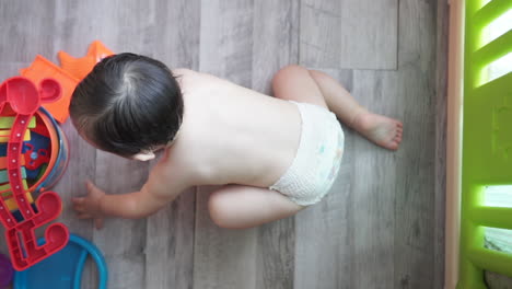 High-angle-shot-of-a-one-year-old-asian-kid-calmly-playing-by-himself-with-colorful-plastic-balls-and-toys-wearing-only-a-diaper