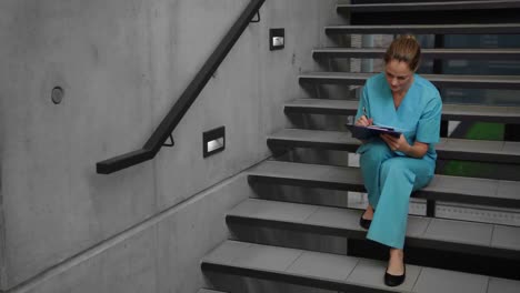 nurse sitting on steps and writing on clipboard