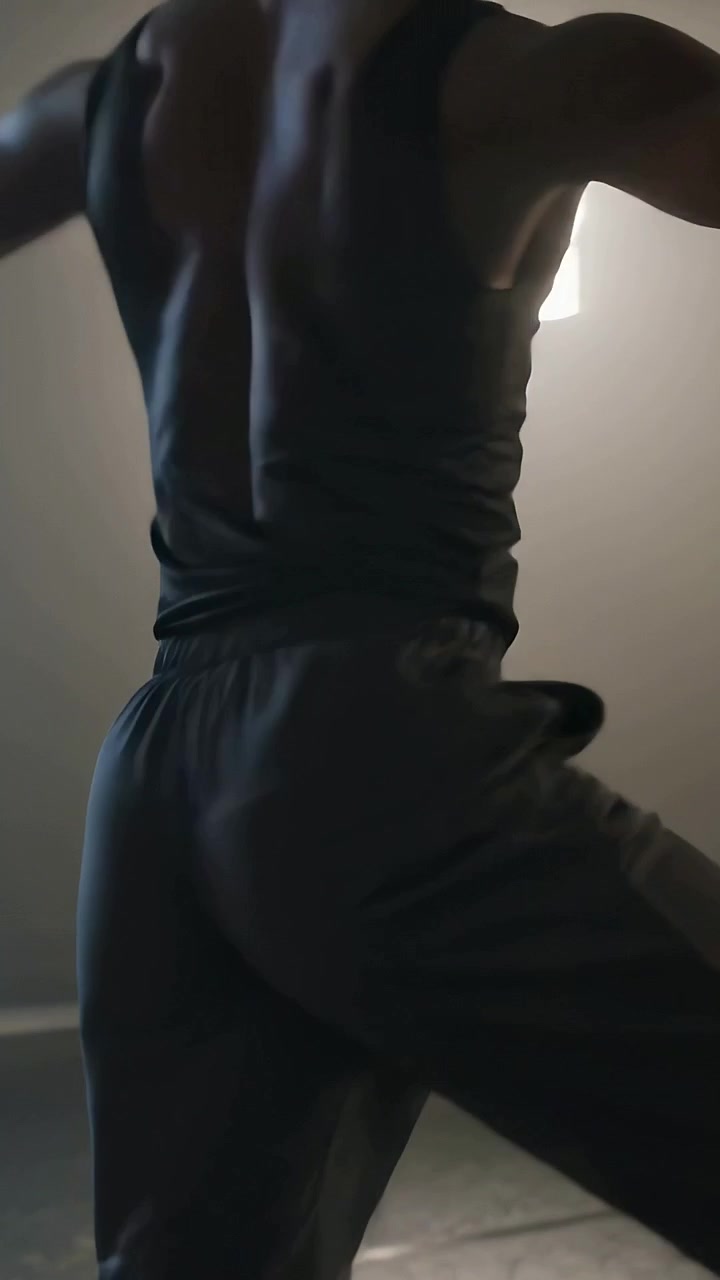 Video verticale: Uomo che si allena con canotta nera e pantaloni scuri, eseguendo movimenti di anca e gambe in una stanza illuminata.