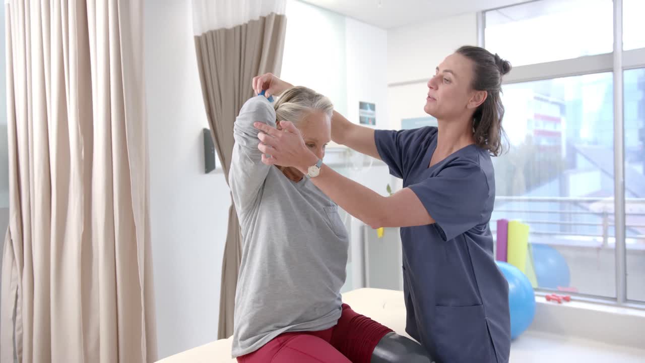 백인 여성 물리 치료사가 여성 노인 환자에게 저항 밴드로 운동을 도와줍니다.
