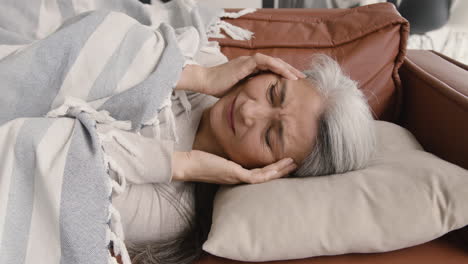 sick middle aged woman having headache while lying on the couch covered with a blanket