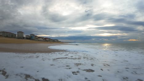 Vuelo-A-Baja-Altura-Sobre-Las-Olas-En-La-Playa-De-Surf-De-Hossegor-Durante-Una-Puesta-De-Sol-Nublada