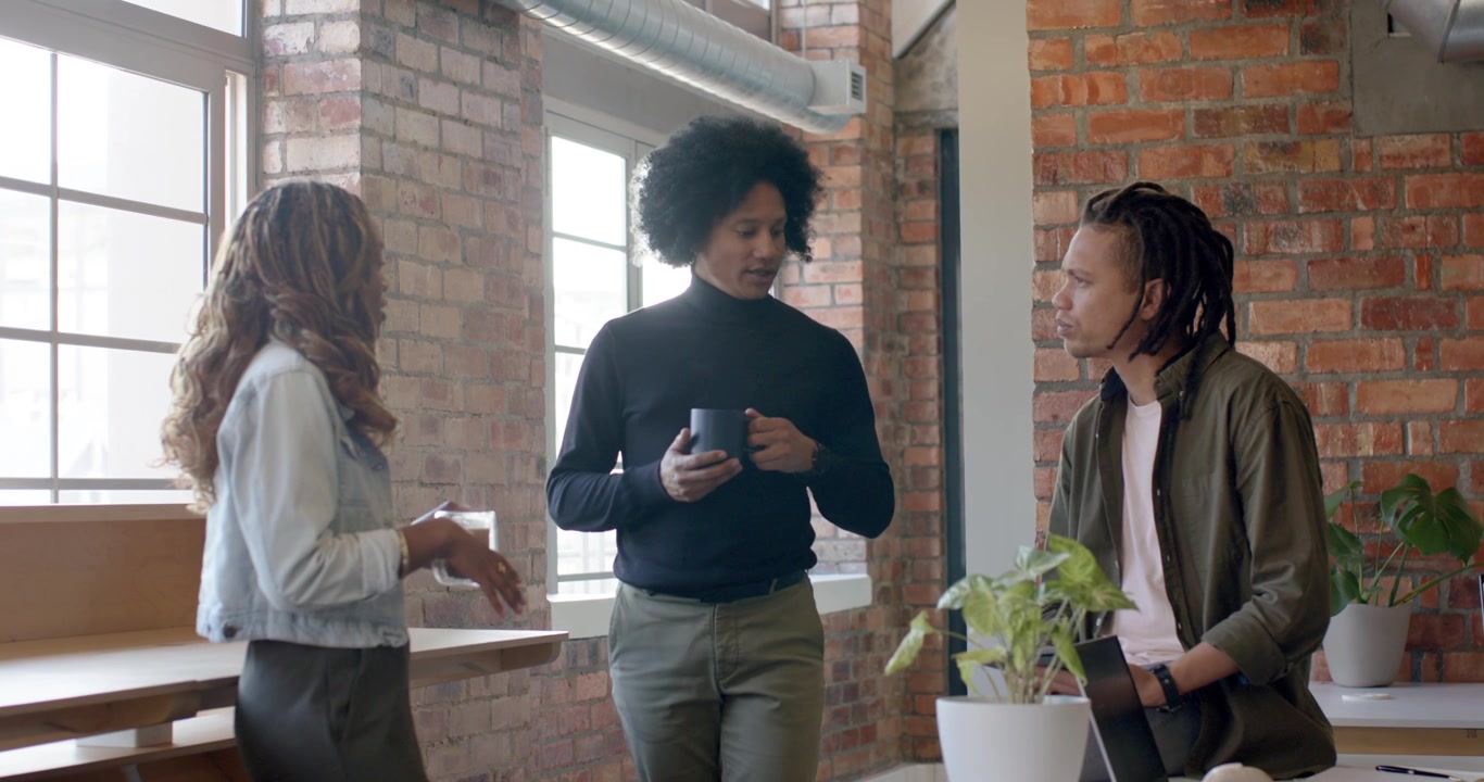 African American coworkers chatting in loft, woman gesturing, center man holding mug listening