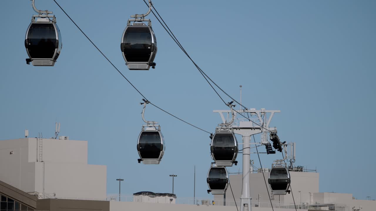 Diverse gondole Yokohama Air Cabin che viaggiano lungo un sistema di funivia sopra la città a Minato Mirai, Yokohama, in una giornata limpida e soleggiata, mostrando le moderne infrastrutture di trasporto aereo urbano.