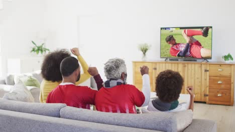 african american family watching tv with diverse male soccer players playing match on screen