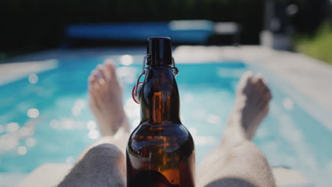 맥주 한 병 을 들고 있는 한 사람 이 뜨거운 여름 날 에 수영장 근처 에서 휴식을 취하고 있다. 느린 동작 비디오