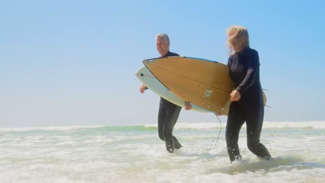 vista frontal de una pareja caucásica senior activa corriendo en el mar en la playa 4k
