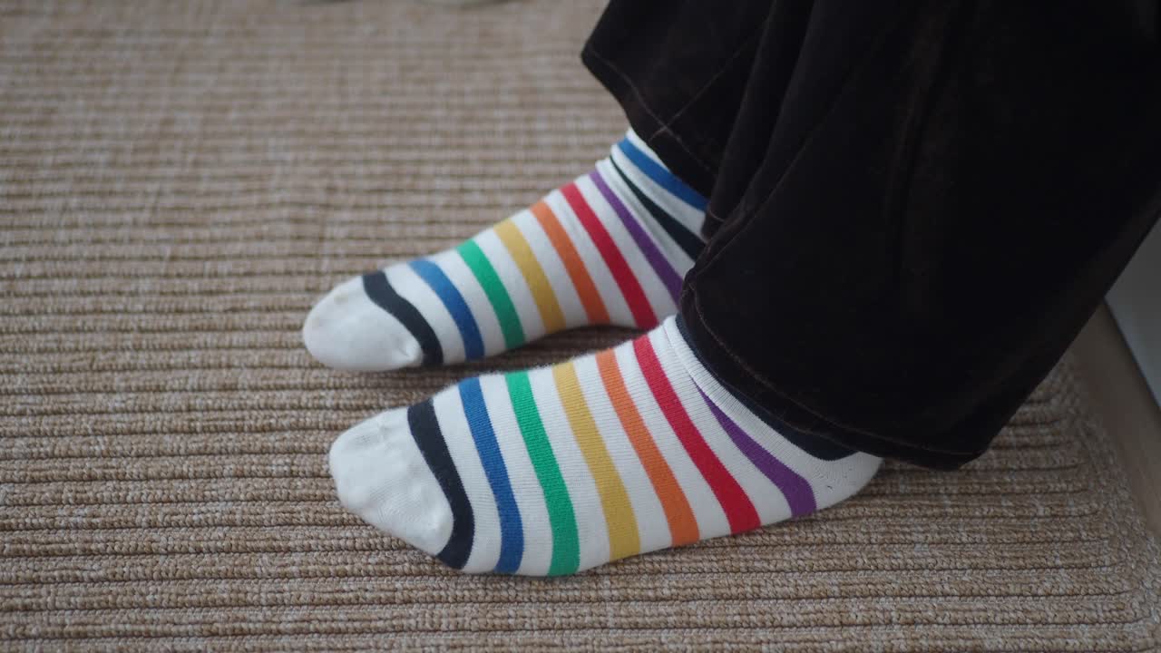 Persona che indossa calzini a strisce arcobaleno colorate su un tappeto.