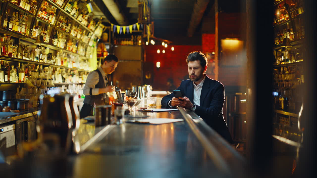 Un cliente del bar controlla un SMS sul cellulare mentre si rilassa al bancone. Un uomo beve un cocktail