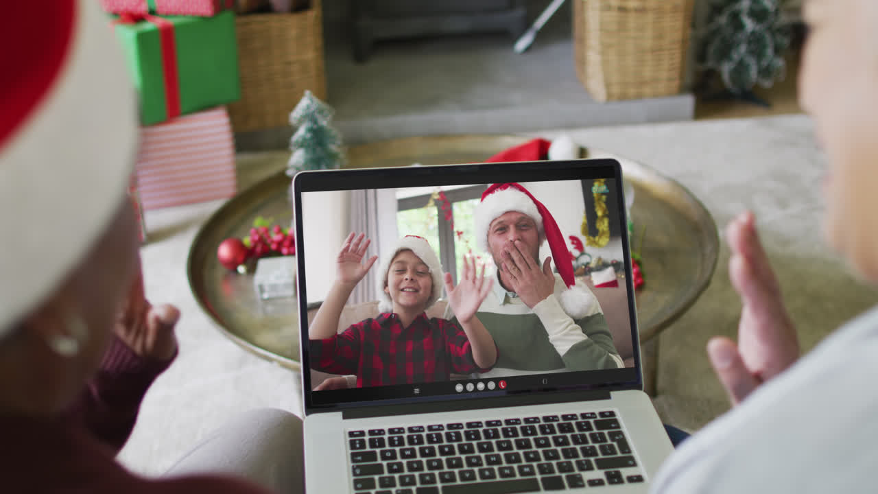 diversas amigas mayores que usan una computadora portátil para una videollamada de navidad con una familia feliz en la pantalla
