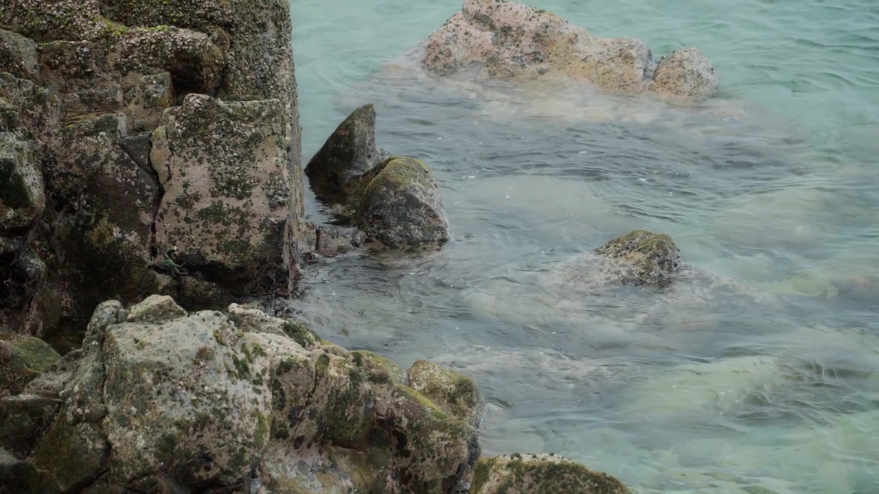 Inquadratura statica di acqua oceanica calma che si muove intorno a rocce costiere.