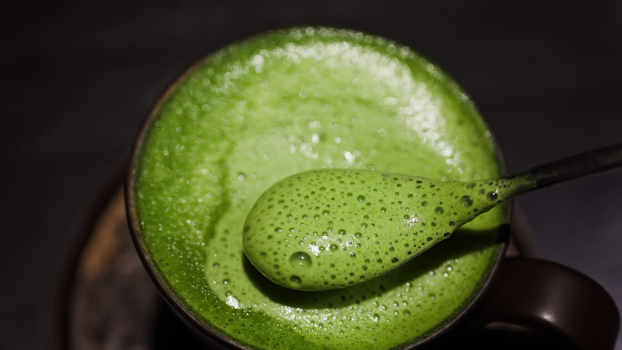 Close up of a spoon mixing into a matcha latte on a tray at a cafe