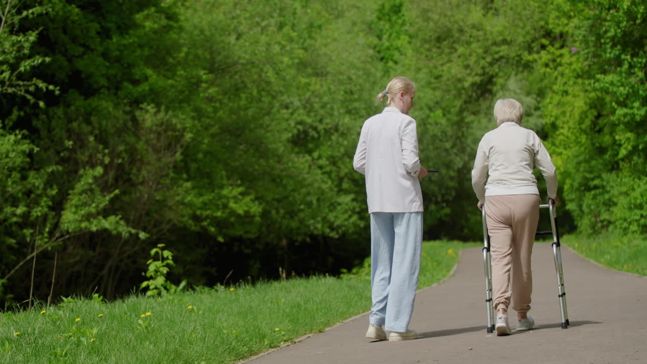 Eldre kvinne går med hjelp i park