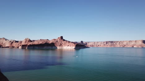 aerial shot flying past a shadow covered mountain to reveal a houseboat sitting on lake powell