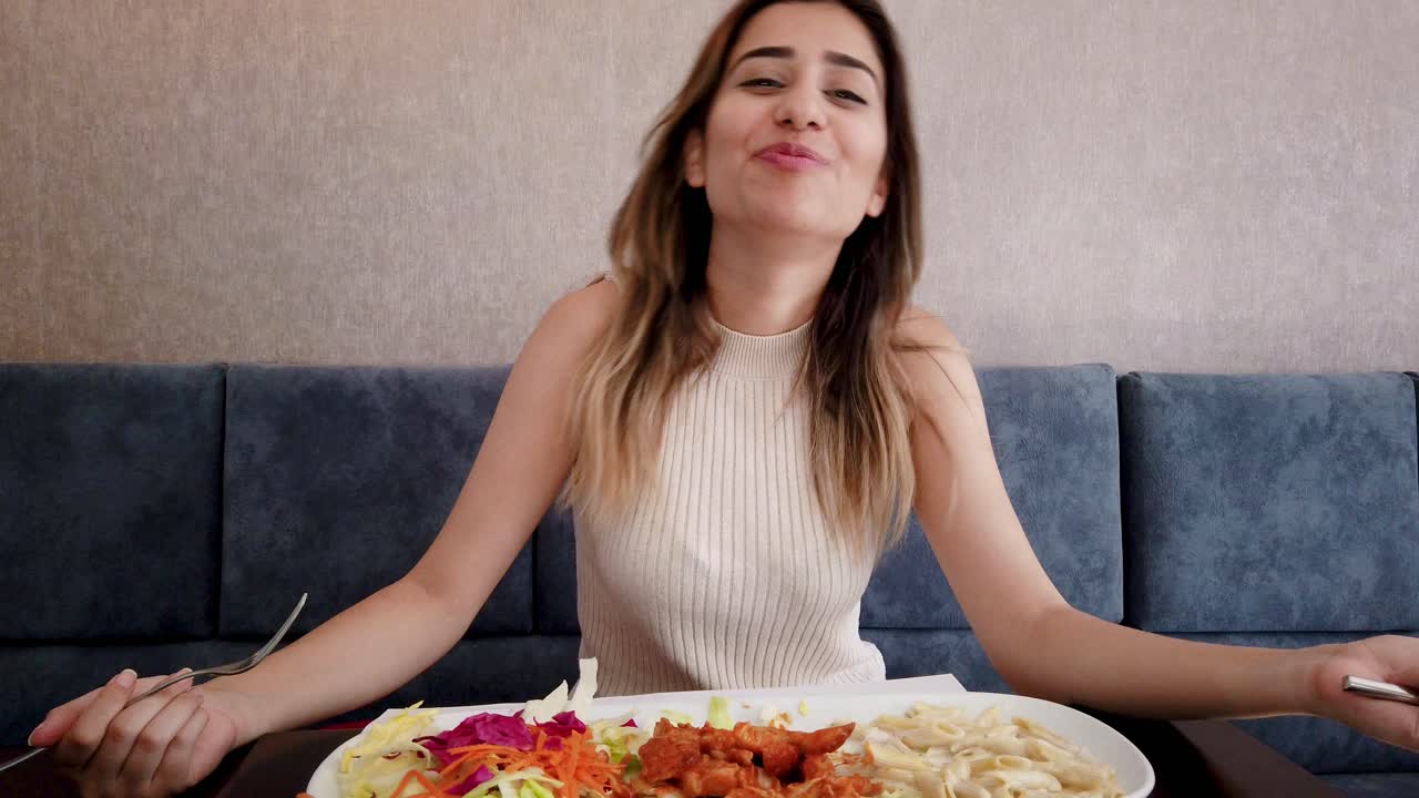 cámara lenta: hermosa joven come comida de pollo con un gran disfrute en un restaurante o cafetería mientras está sentada