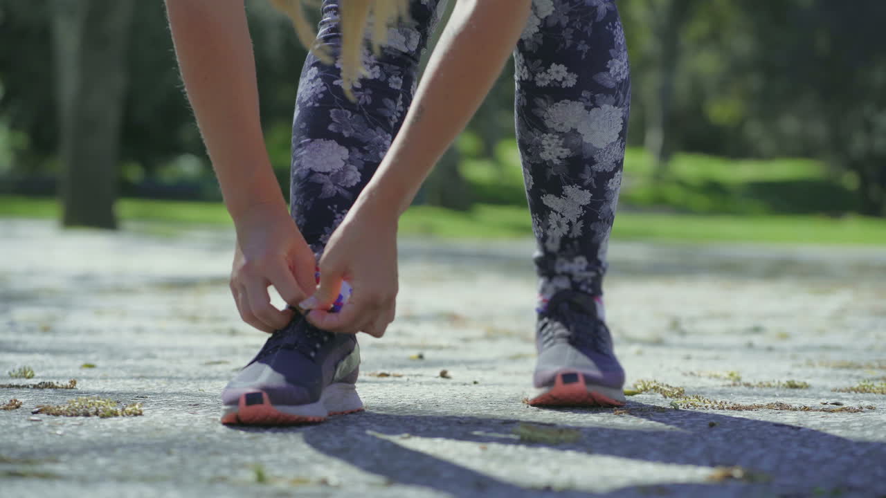 Giovani gambe e mani femminili che allacciano i lacci delle scarpe da corsa.
