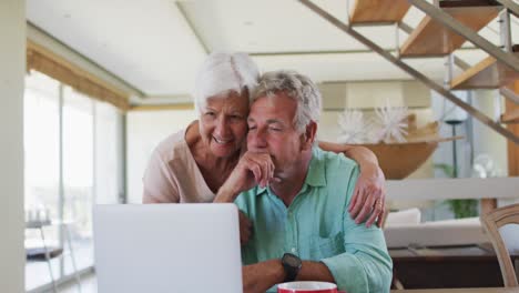 Glückliches-älteres-Kaukasisches-Paar,-Das-Miteinander-Redet,-Während-Es-Zu-Hause-Gemeinsam-Einen-Laptop-Benutzt