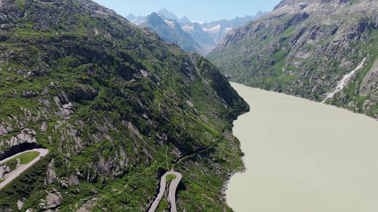 Un'inclinazione aerea verso l'alto rivela la tortuosa strada del Grimsel accanto a un latteo bacino alpino svizzero.