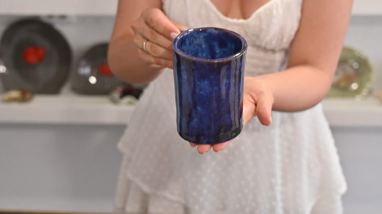 Donna in abito bianco che presenta una tazza blu in cucina
