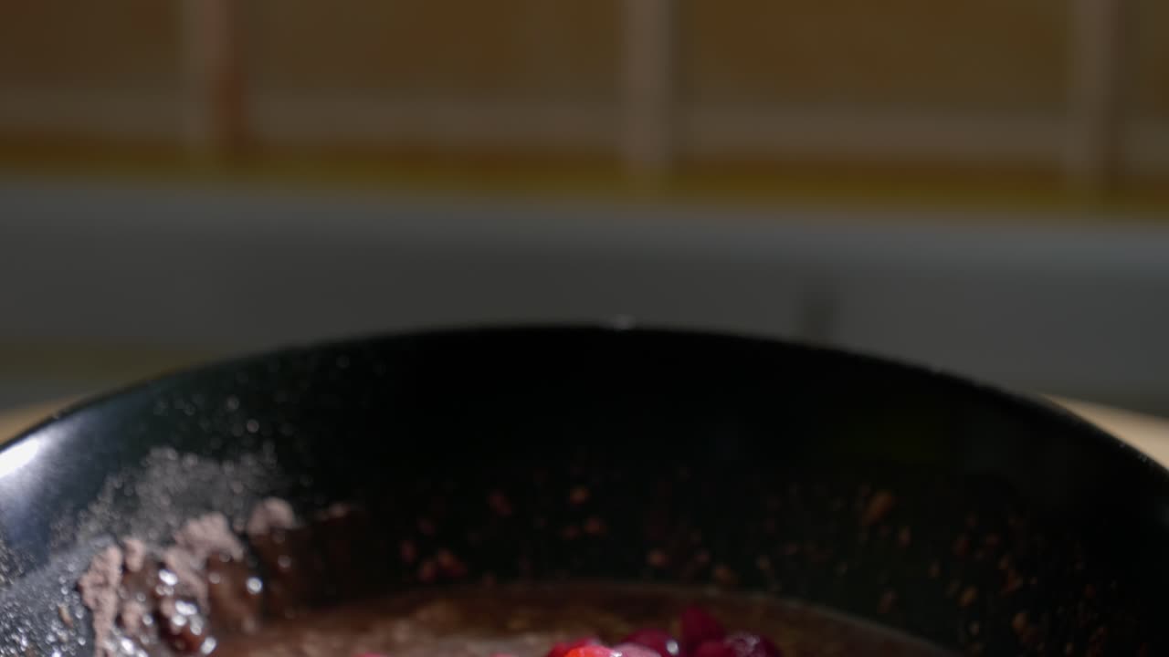 A tilt shot panning down to reveal a low calorie protein pudding topped with a generous helping of tasty red currants served in a black dessert bowl