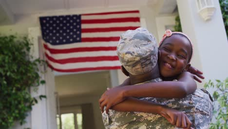 Afroamerikanischer-Soldatvater-Umarmt-Lächelnde-Tochter-Vor-Dem-Haus-Mit-Amerikanischer-Flagge