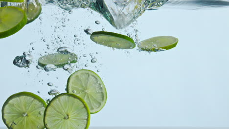 closeup lime slices underwater on white background. citrus falling under water.