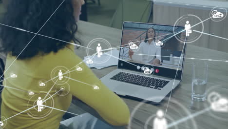 animation of network of connections with icons over biracial businesswoman using laptop in office