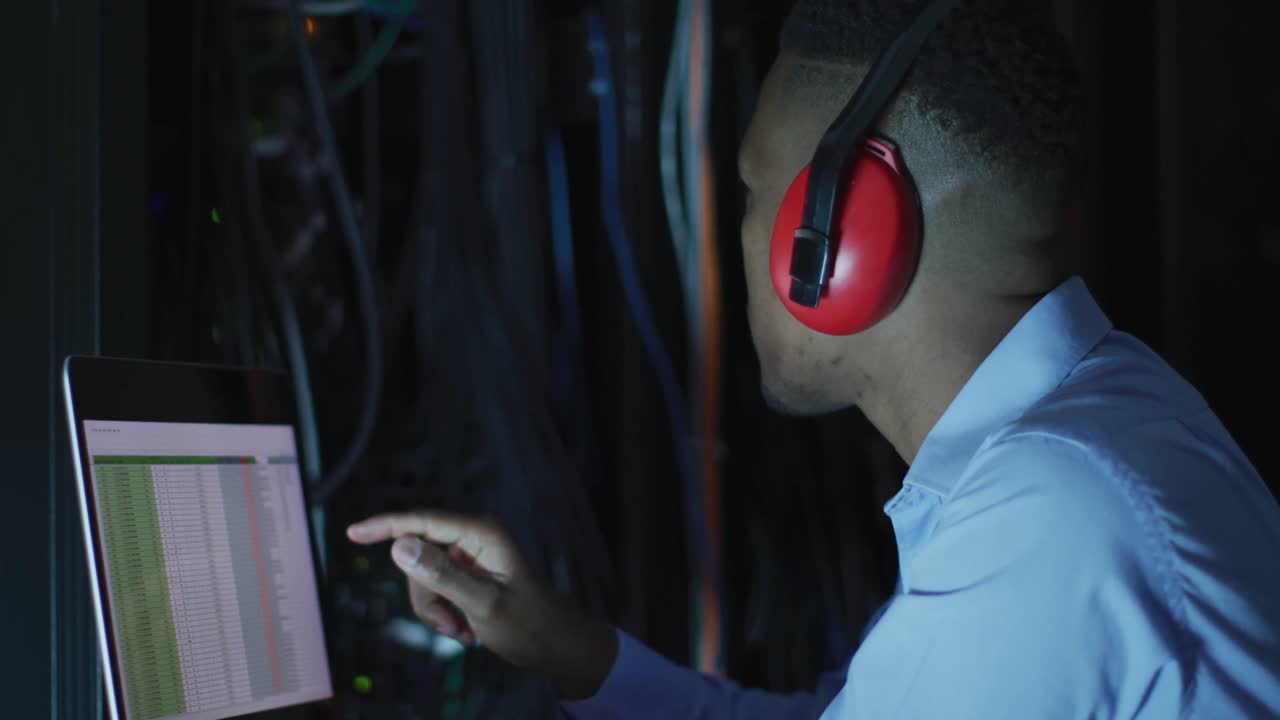 técnico informático afroamericano que usa una computadora portátil trabajando en una sala de servidores de negocios