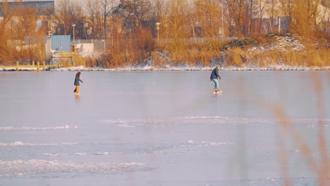 Gente-Patinando-Sobre-Hielo-En-Agua-Congelada-Al-Aire-Libre-Con-árboles-De-Otoño-En-Segundo-Plano