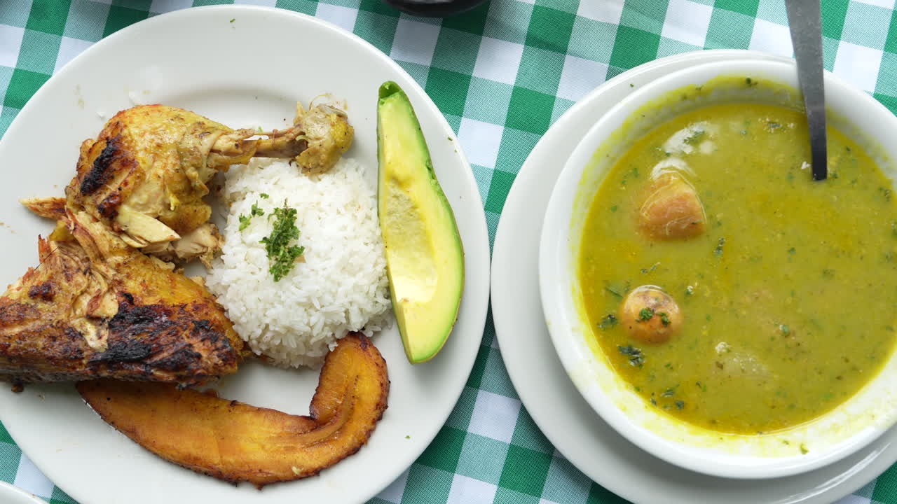 Close-up de delicioso sancocho de gallina colombiano com arroz, abacate e banana da terra frita sobre uma toalha de mesa xadrez vibrante. Refeição quente e convidativa sob iluminação natural suave.