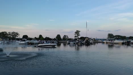 Boat-leaving-the-marina-to-go-tubing-with-a-beautiful-fountain-water-feature-in-frame-at-Lake-Geneva,-Wisconsin