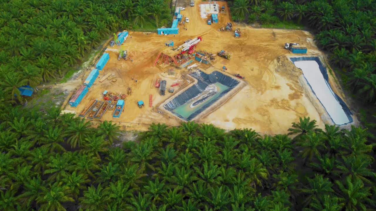 imágenes cinematográficas de drones de la estructura del equipo de la plataforma de perforación en tierra para la exploración y explotación de petróleo en medio de la jungla rodeada de palmeras durante la puesta de sol y el alto precio del petróleo