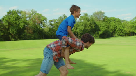 Man-and-boy-playing-in-meadow.-Father-giving-son-piggyback-riding-outdoors