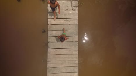 Aerial-view-of-a-group-of-indigenous-children-running-in-a-river-wooden-pier