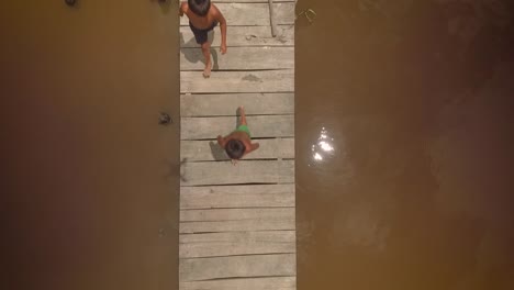 Vista-Aérea-De-Un-Grupo-De-Niños-Indígenas-Corriendo-En-Un-Muelle-De-Madera-De-Río