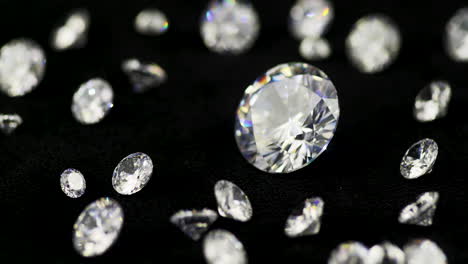 Echter-Großer-Glitzernder-Diamant-Im-Brillantschliff,-Umgeben-Von-Den-Kleineren,-Die-Sich-Im-Uhrzeigersinn-In-Geringer-Schärfentiefe-Auf-Dem-Schwarzen-Tisch-Drehen---Filmische-Nahaufnahme-Mit-Selektivem-Fokus