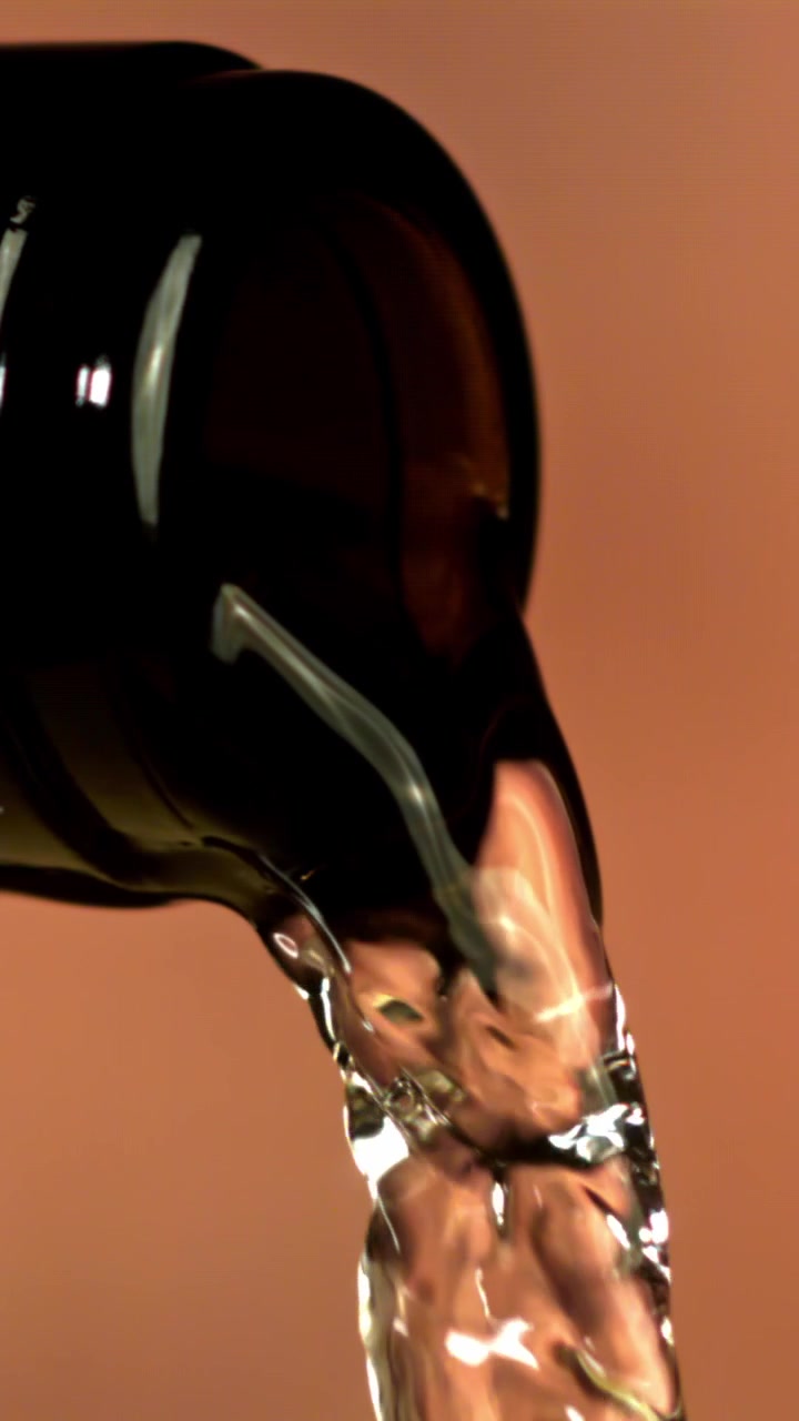 Primo piano di liquido trasparente che si versa da una bottiglia scura.