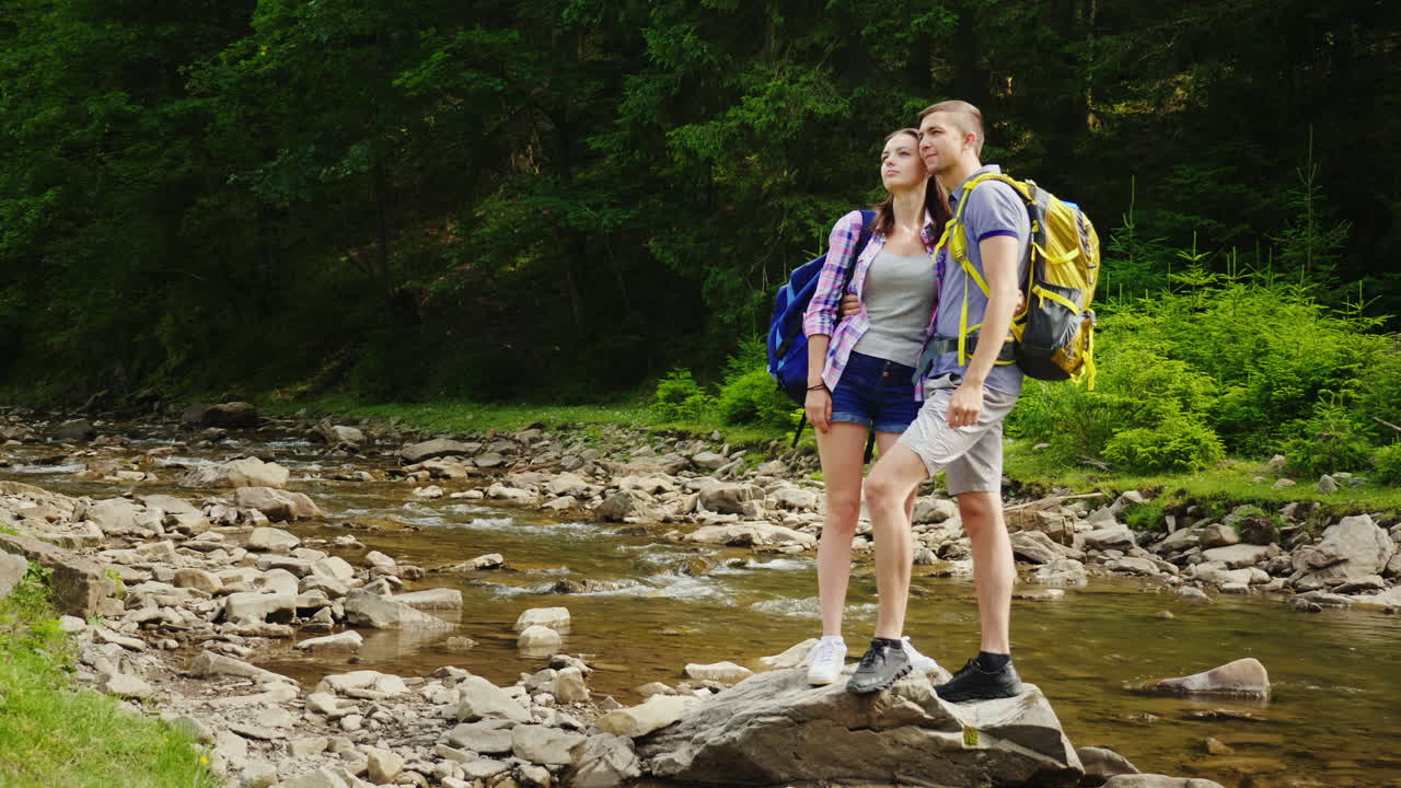 una pareja amorosa de turistas con mochilas descansa en un lugar pintoresco cerca de un río de montaña que e