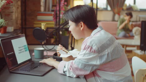 asian woman eating and working on laptop at home