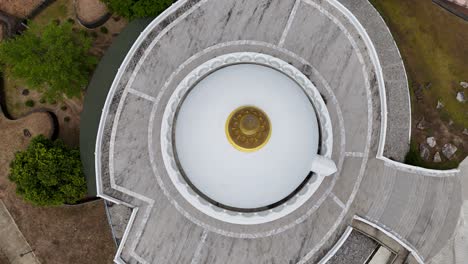 drone footage captures a circular buddhist temple in phuket, thailand, showcasing its architectural design and surrounding greenery