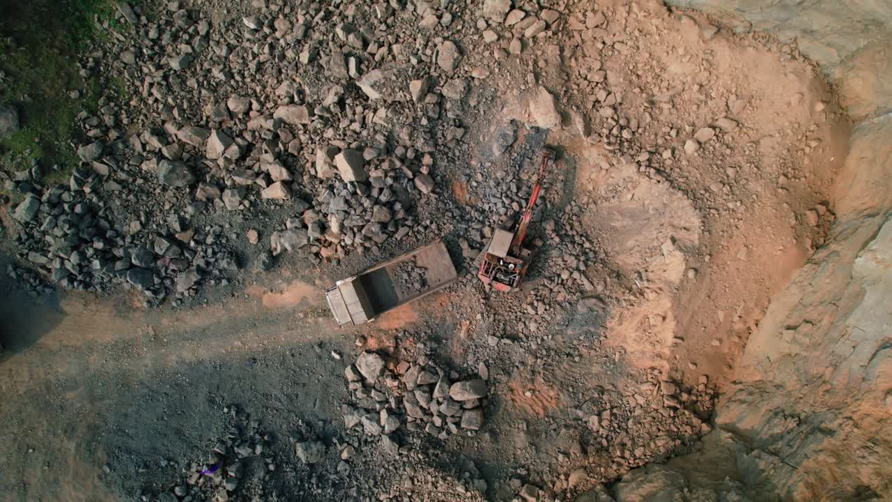 Top rotating drone view of Excavator loads ore into a large mining dump truck. Top view. Open-pit. Aerial view of an excavator loading paving stones into a dump truck on the street of the old town
