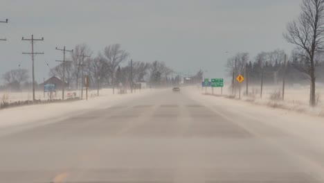 snowy winter road while wind blowing snow particles, driving pov view