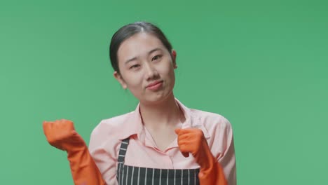 primer plano de una alegre ama de casa asiática con un delantal bailando mientras está de pie en el estudio de pantalla verde