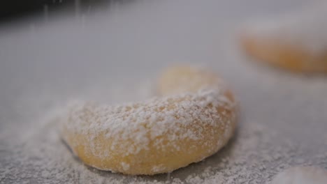 close-up of freshly baked vanilakipferl cookies as powdered sugar sprinkles down on top