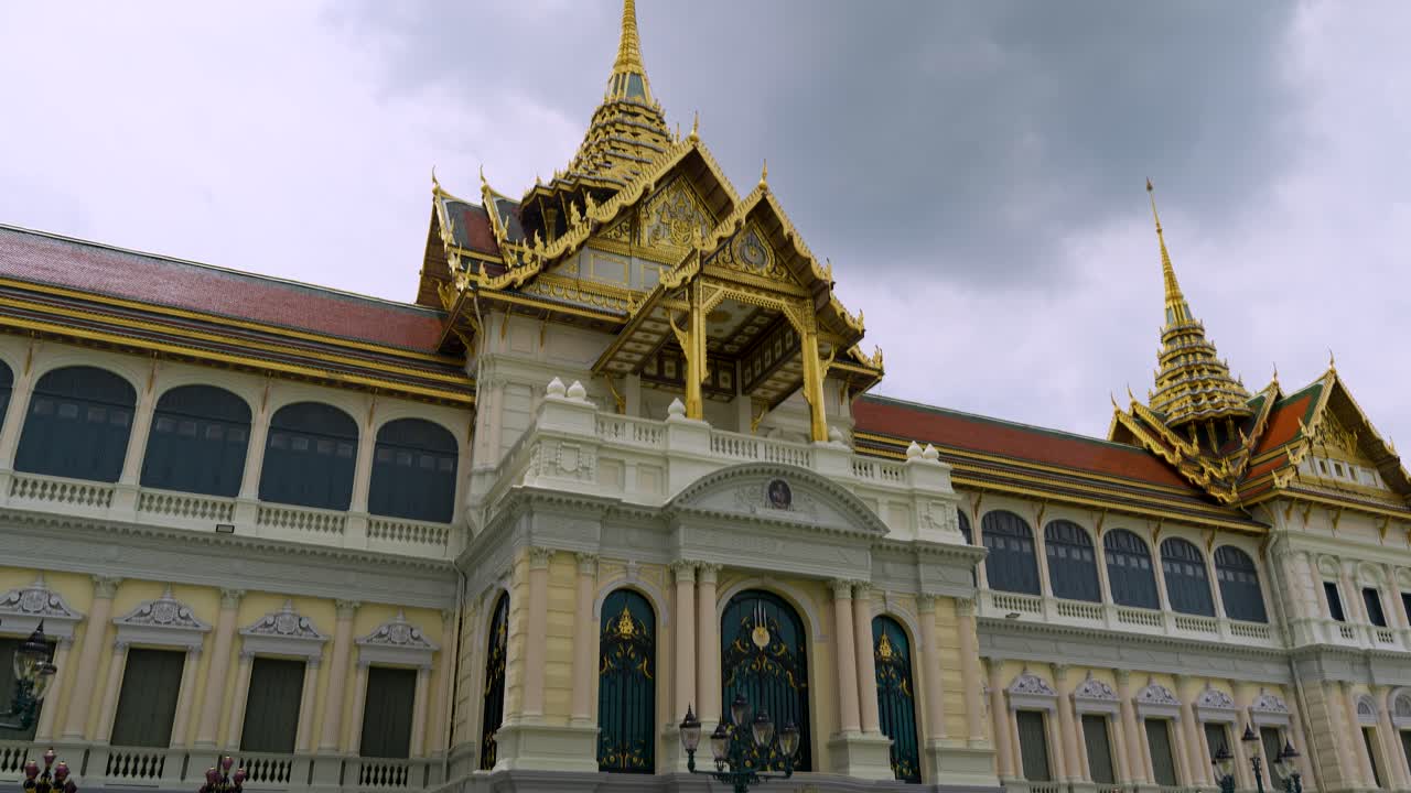 Inquadratura a mano, verso il basso, che svela un sontuoso palazzo dal tetto dorato nel complesso del Grande Palazzo Reale a Bangkok, Thailandia, con architettura dettagliata e guglie.
