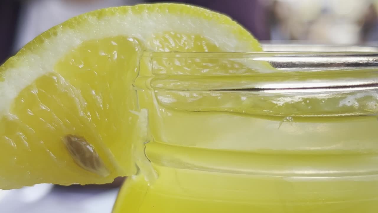 primer plano de una rodaja de limón amarillo en el borde de un frasco de vidrio lleno de limonada.