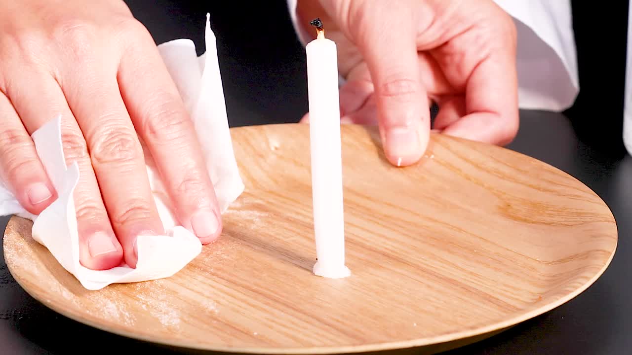 Close-up of hands wiping a wooden plate with a candle using a cloth.