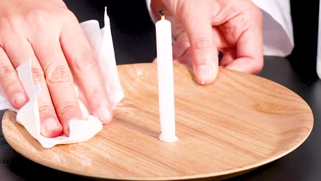 close-up of hands wiping a wooden plate with a candle using a cloth.